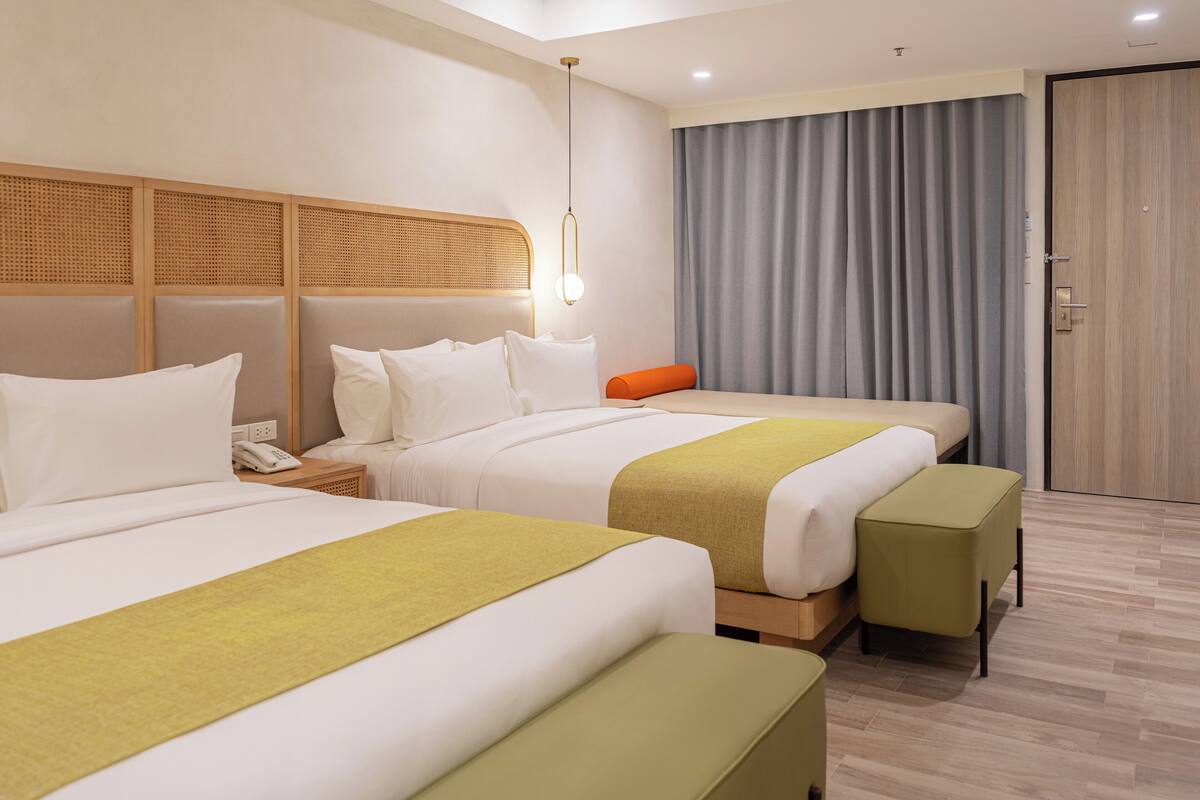 Een hotelkamer met twee bedden, een houten hoofdbord, een nachtkastje met een telefoon en een groot raam met gordijnen.