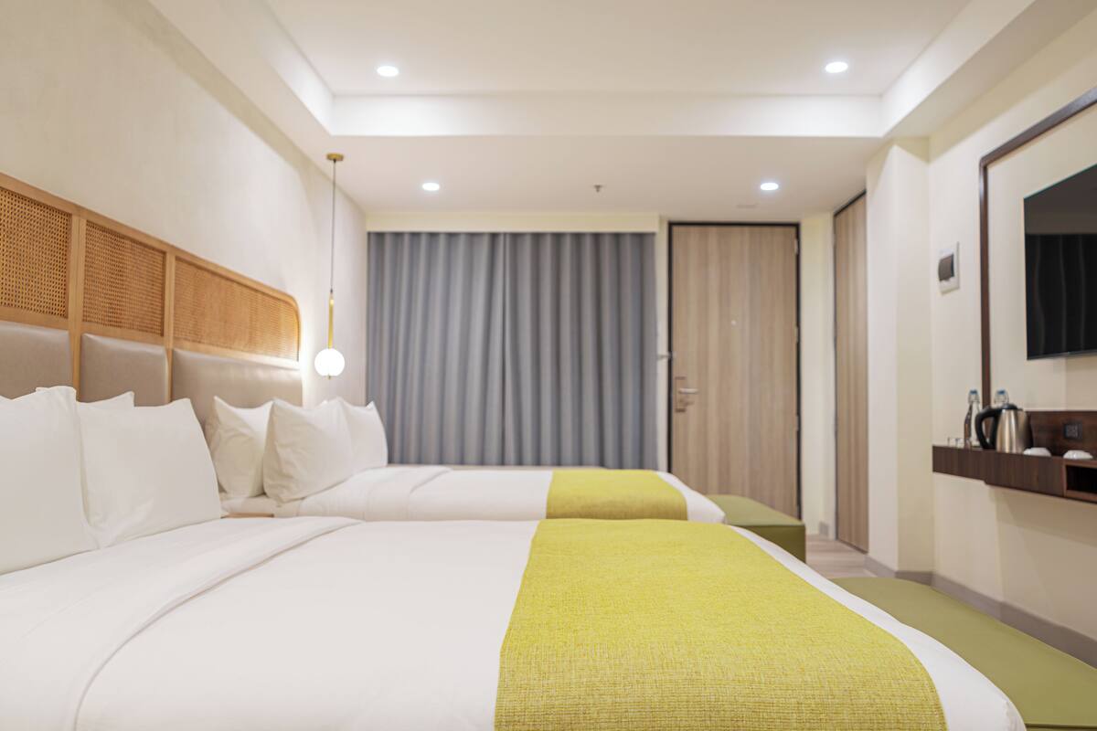 Een hotelkamer met twee bedden, een groot raam met gordijnen, een houten hoofdbord, een nachtkastje met een lamp en een spiegel aan de muur.
