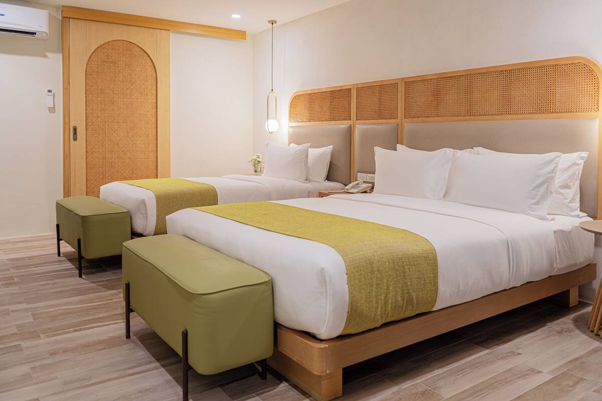Hotelkamer met twee bedden, een houten hoofdbord, een nachtkastje met telefoon en een klein groene voetenbankje.
