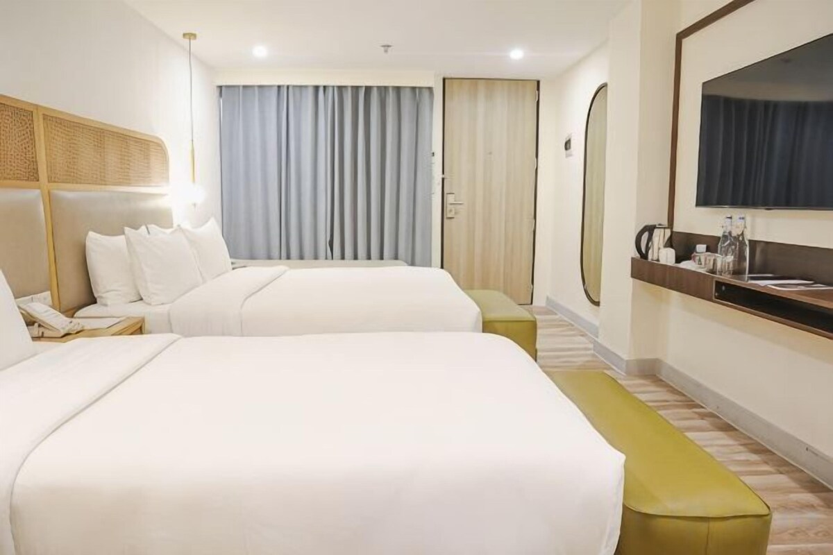 Een hotelkamer met twee bedden, een bankje, een nachtkastje met telefoon, een spiegel en een raam met gordijnen.