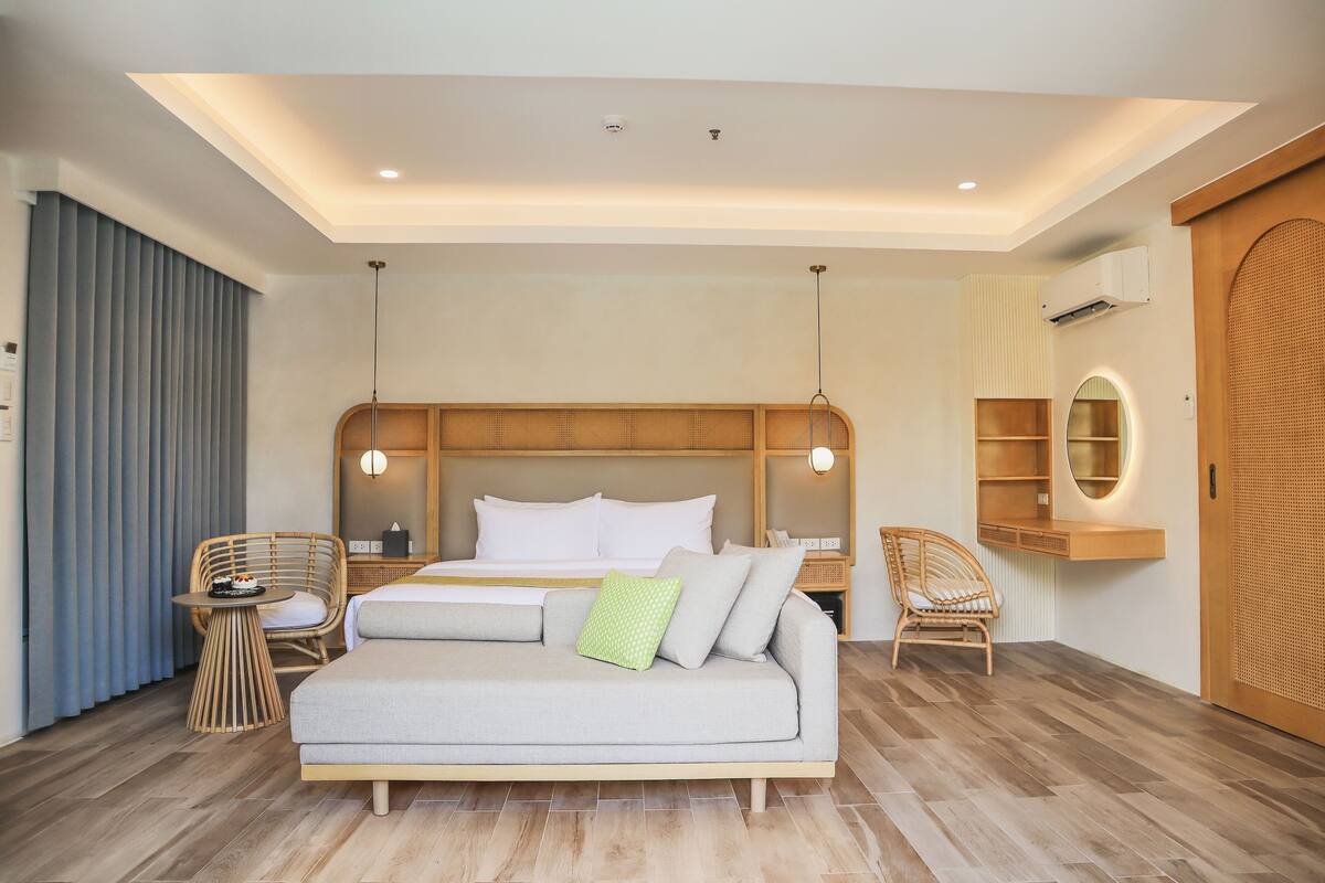 Een moderne hotelkamer met een groot bed, een slaapbank, twee rieten fauteuils, een bijzettafeltje en een houten garderobe.