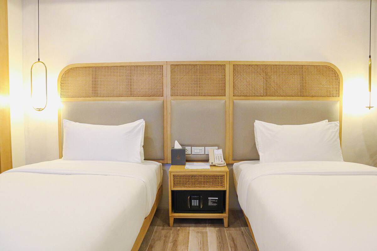 Een hotelkamer met twee bedden, een houten hoofdbord, een nachtkastje met een telefoon, een lamp en een bedieningspaneel.