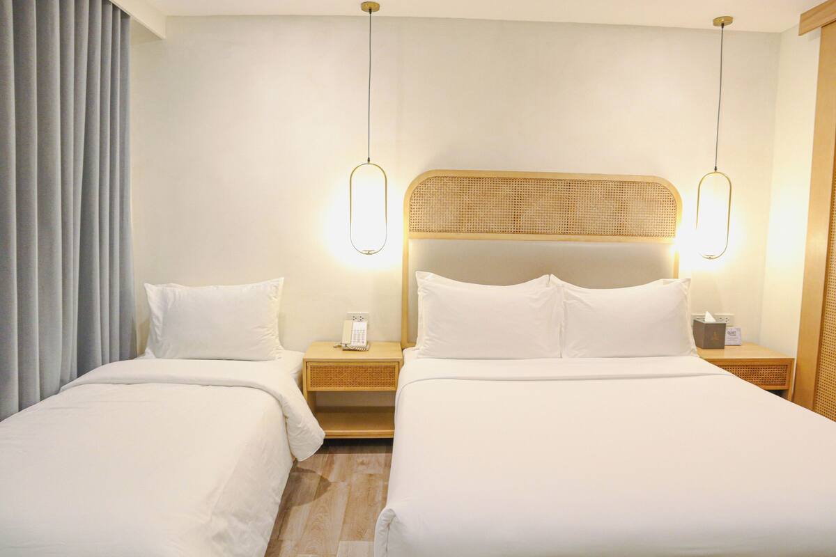 Een hotelkamer met twee bedden, een nachtkastje met een lamp, een telefoon en een wandlamp.