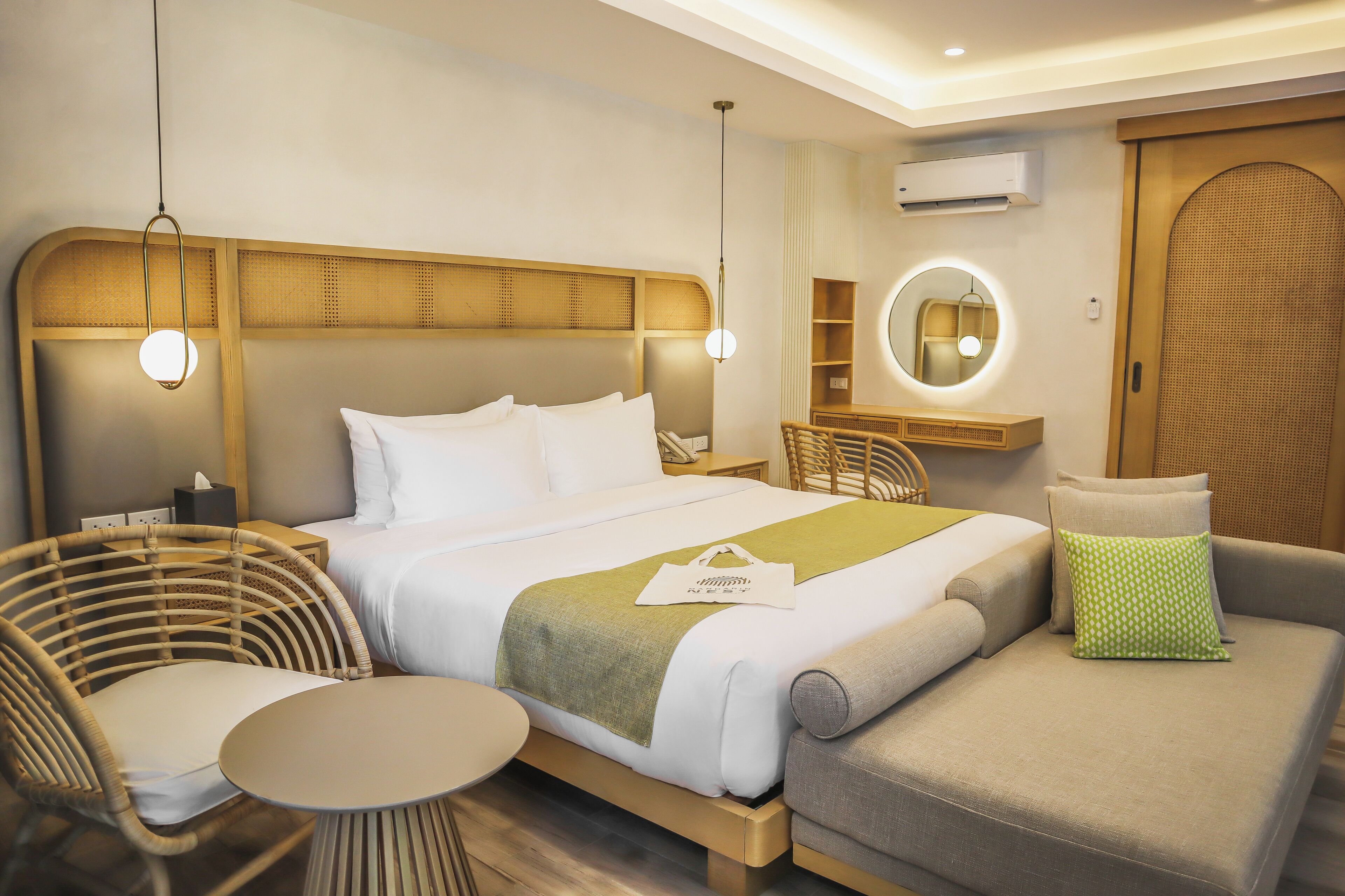 A modern hotel room with a bed, a round mirror, a small table, and a seating area.