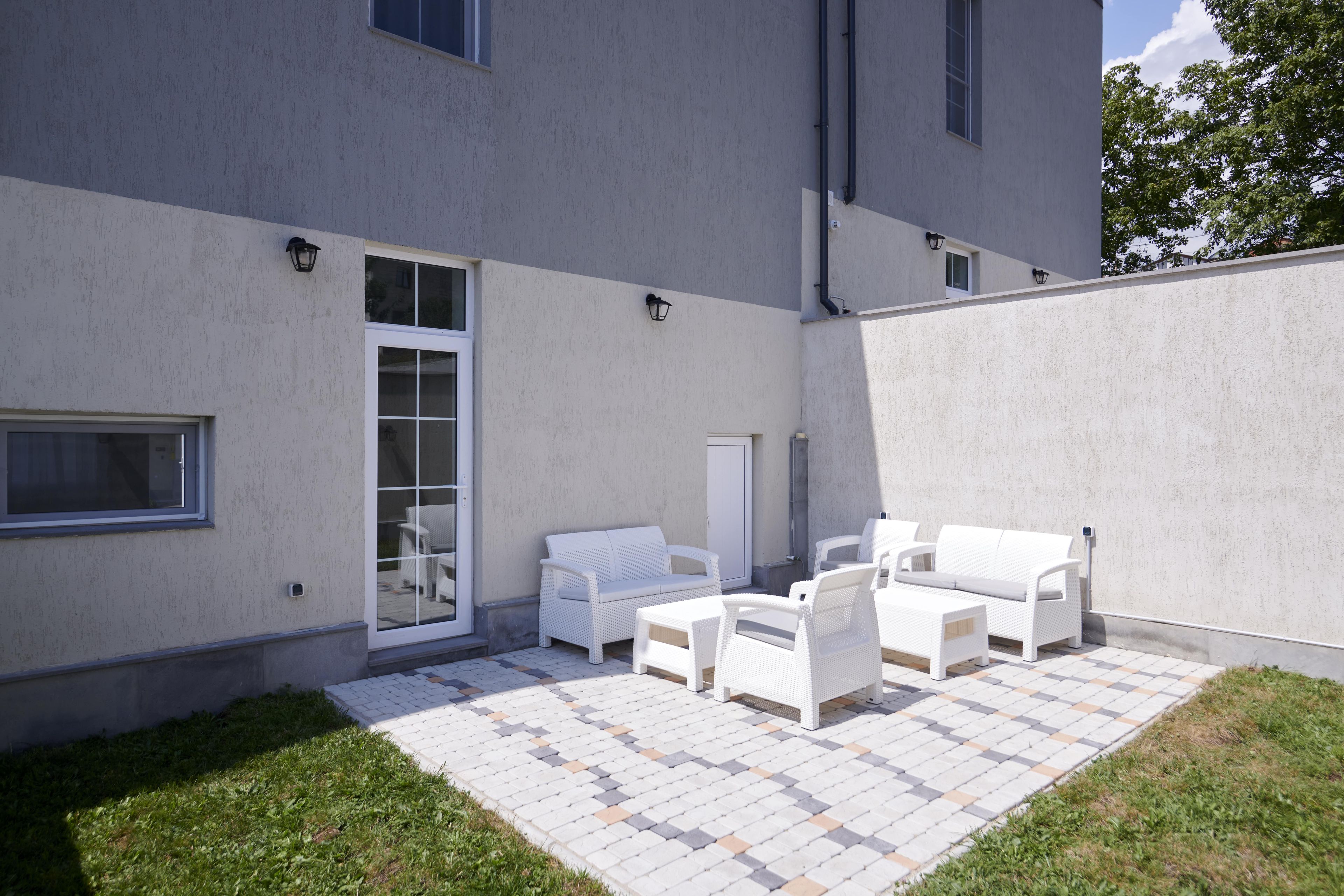 A patio area with white outdoor furniture, a sliding glass door, and a paved floor.