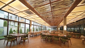 A spacious indoor dining area with wooden tables and chairs, large windows, and a ceiling with wooden slats.
