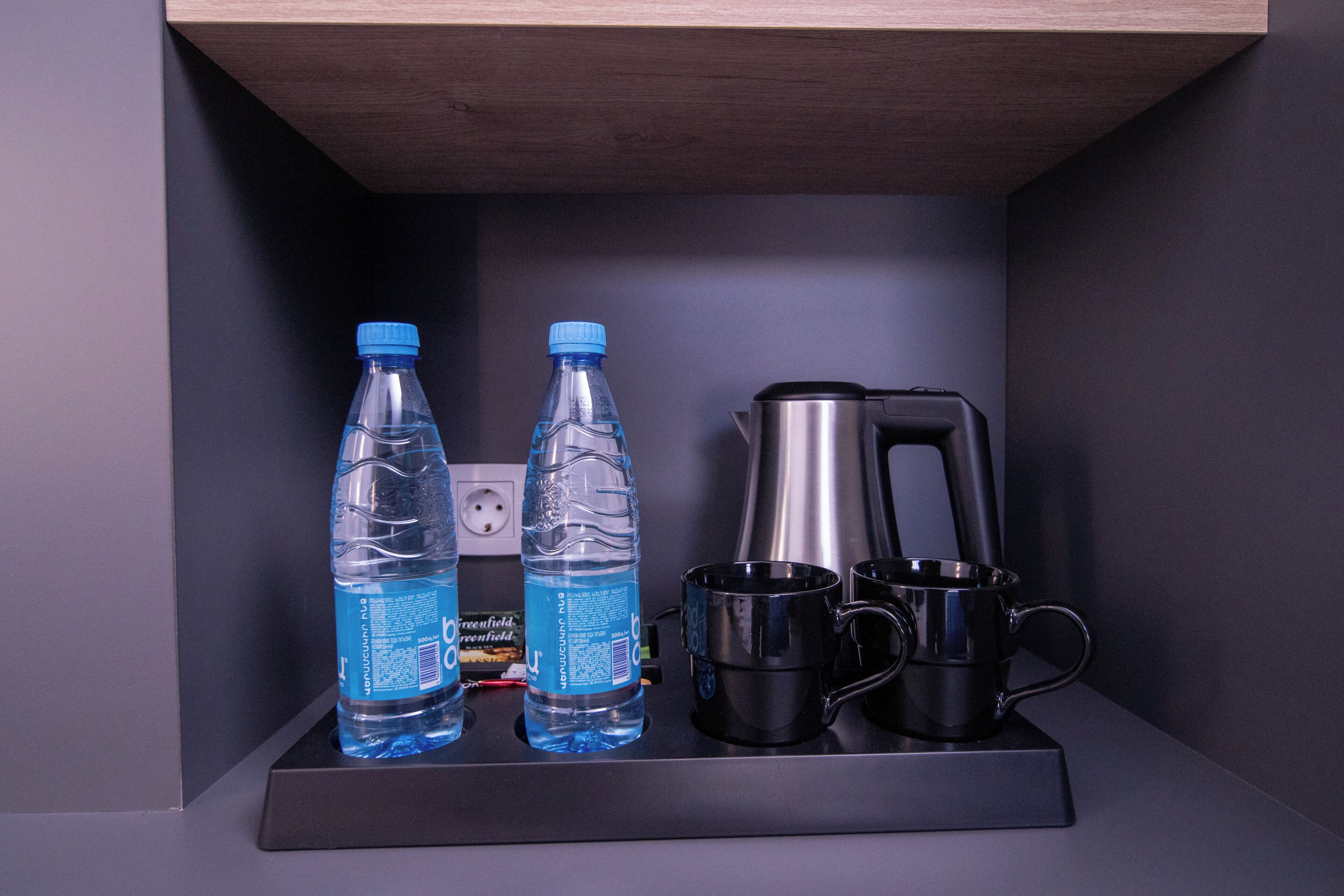 Ein Regal mit zwei Wasserflaschen, einer Kaffeemaschine und zwei schwarzen Tassen.