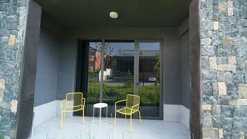 A modern building entrance with a stone facade, two yellow chairs, and a small table on a tiled patio.