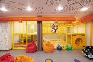 Un área de juegos infantiles con una estructura de juego con red, pufs y un tobogán.