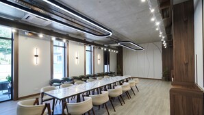 A conference room with a long table and chairs, large windows, and modern lighting fixtures.
