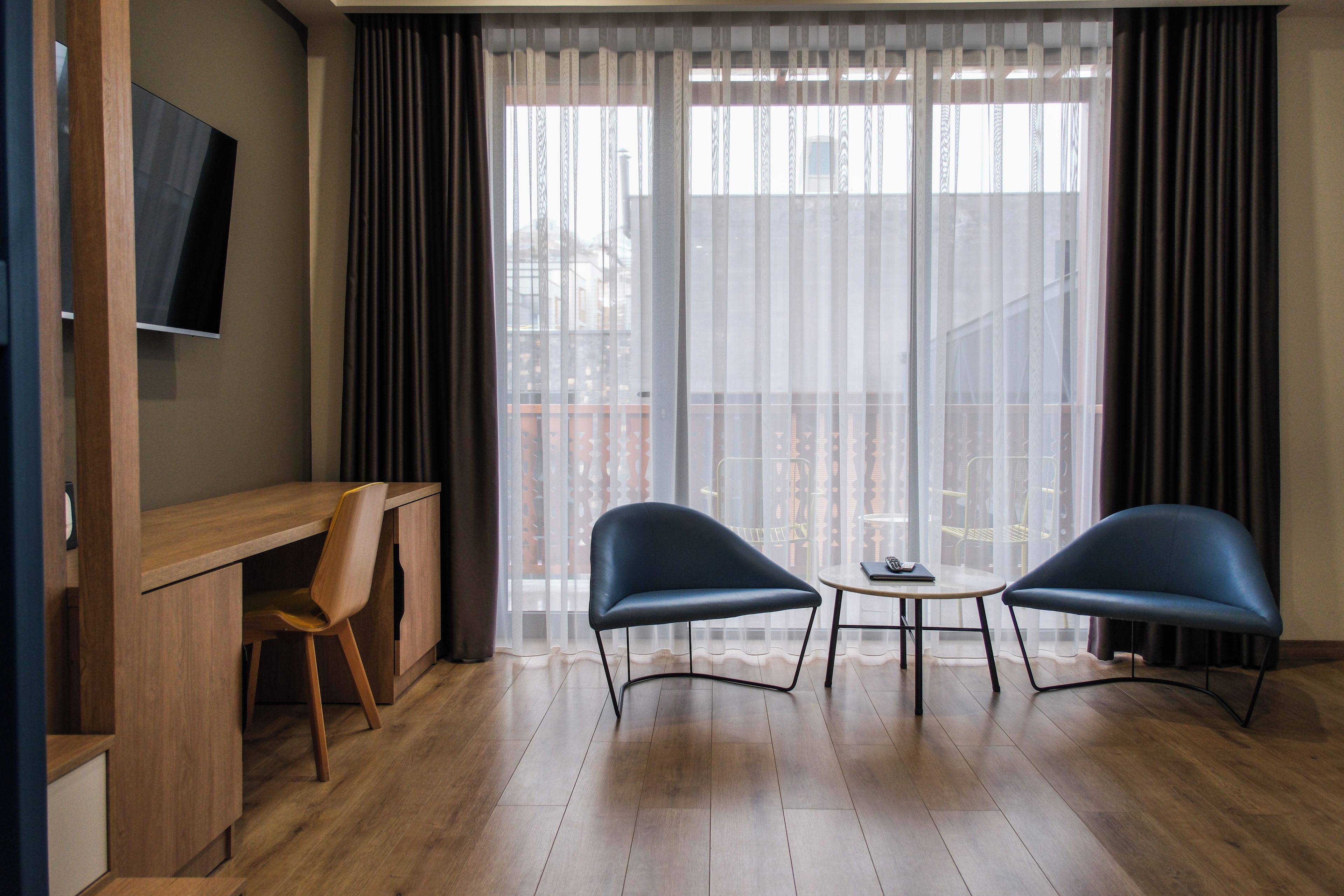 Una habitación moderna con un escritorio de madera, dos sillas, una mesita y un televisor en la pared.
