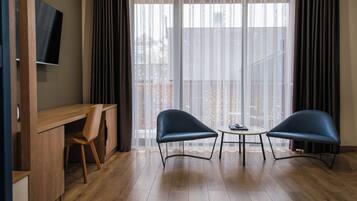 Una habitación moderna con un escritorio de madera, dos sillas, una mesita y un televisor en la pared.