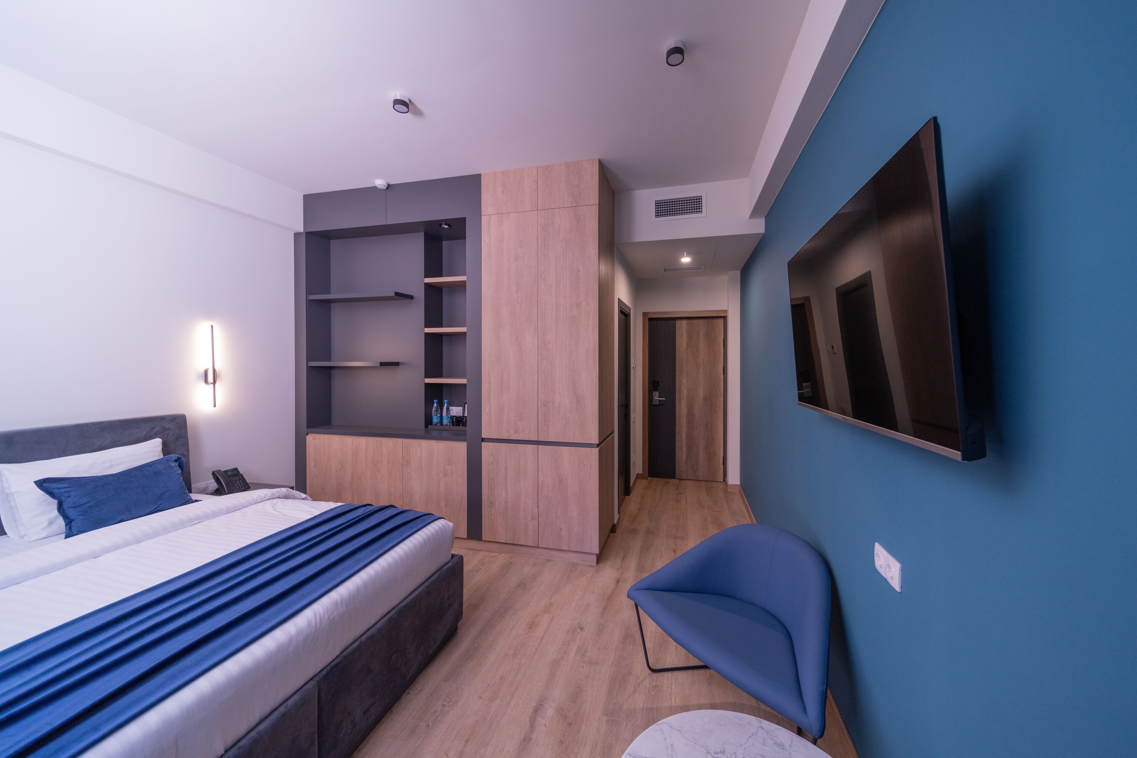 Een moderne hotelkamer met een bed, een inbouwkast, een zithoek en een aan de muur bevestigde televisie.