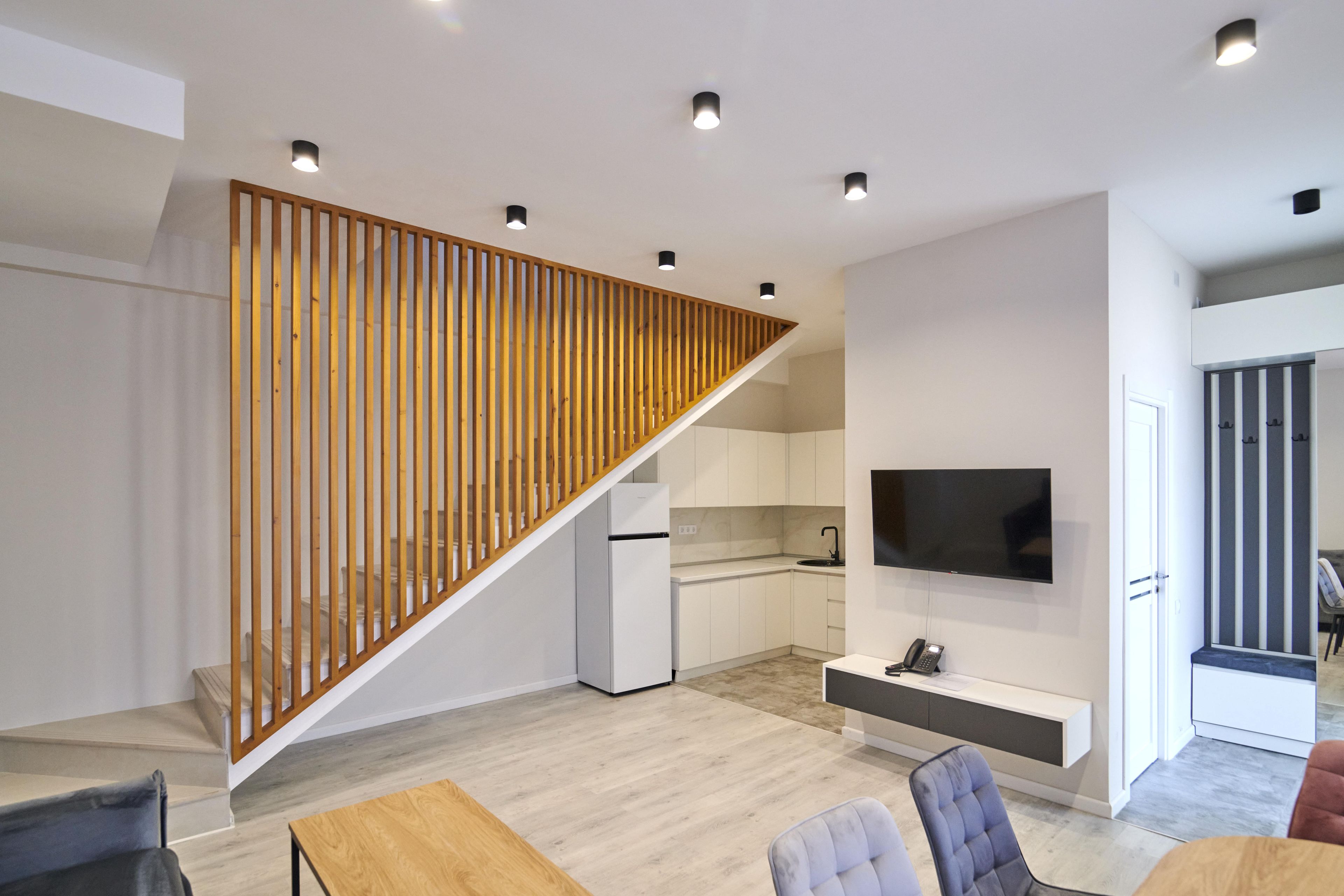 A modern interior with a wooden staircase, a kitchen, a dining area, and a living space with a flat-screen TV.