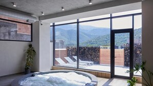 A spa area with a hot tub, large windows, and a view of mountains. - Dili Town Resort and Spa (Dilijan)