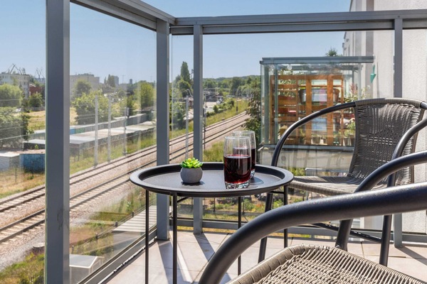 A private balcony equipped with a table and chairs, overlooking a modern urban neighborhood.