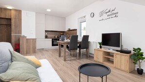 A modern living room with a sofa, a dining table with chairs, a TV, and a small table.