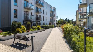 A modern apartment building with balconies, a paved walkway, and a bench.