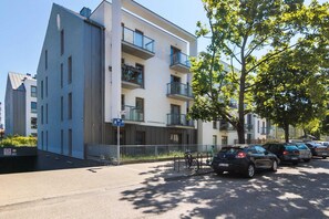 Un immeuble moderne à plusieurs étages, doté de balcons, d’un espace de stationnement et d’un chemin piétonnier.