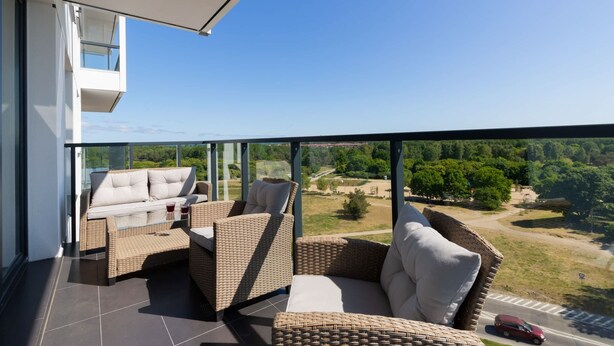 Ein Balkon mit Korbmöbeln und Glasgeländer mit Blick auf eine grüne Landschaft.