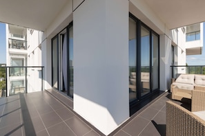 Ein moderner Balkon mit Glastür, Korbmöbeln und Blick auf die Stadt.