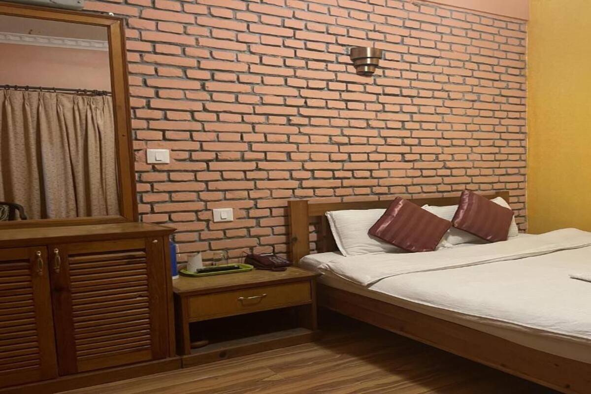 A bedroom with a brick-patterned wall, a wooden bed with white bedding, and a nightstand with a lamp.