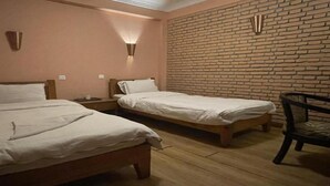 Una stanza con due letti, un muro in mattoni e una sedia.
