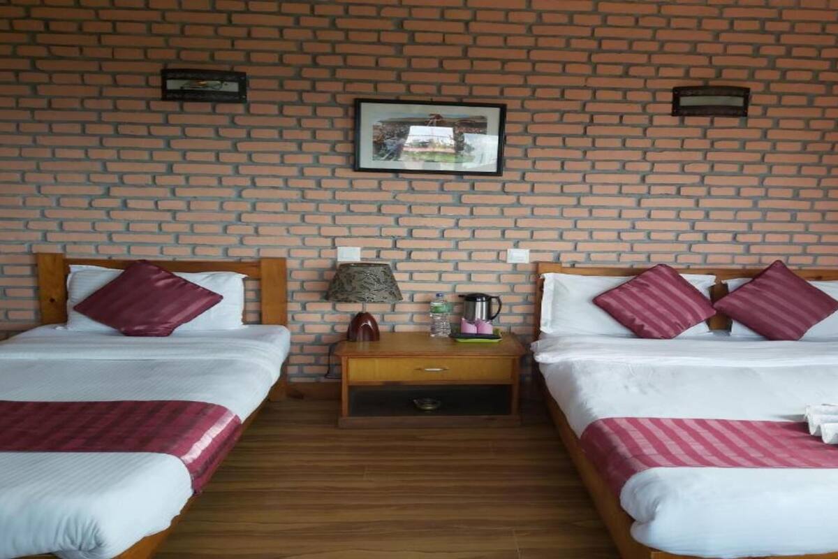 A hotel room with two single beds, a wooden nightstand, a lamp, a framed picture on the wall, and a brick-patterned wall.