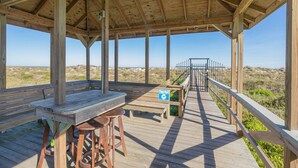 Une terrasse en bois avec une table et des tabourets, un panneau indiquant qu’il faut éteindre les lumières pour ne pas déranger les tortues marines, et une vue sur la plage.