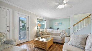 Un salon avec un ventilateur de plafond, une table basse en verre, un canapé beige et un meuble en bois.