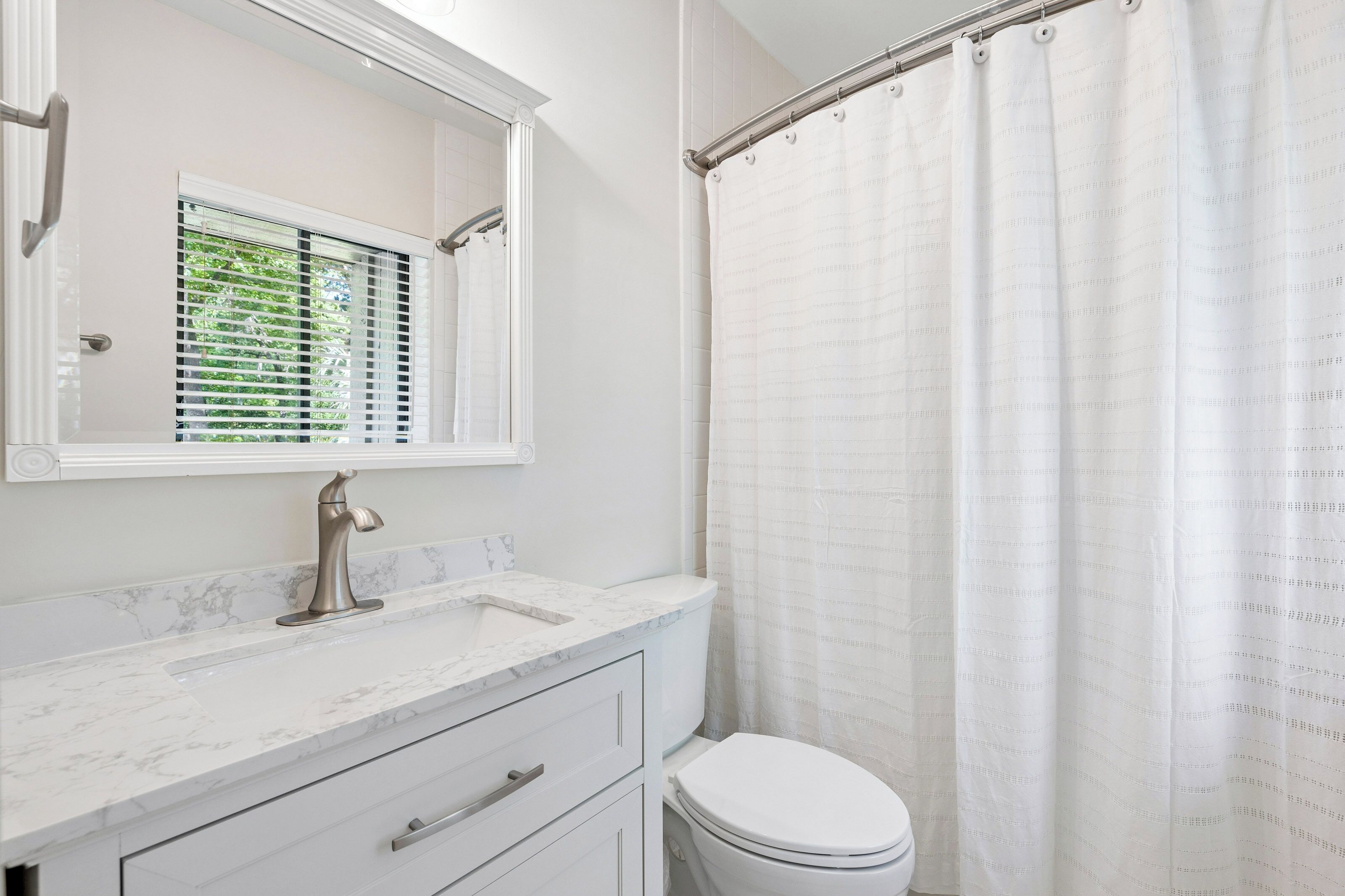 A bathroom with a white toilet, a marble sink, a mirror, and a shower curtain.