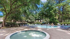 Una piscina con lettini e un'area con vasca idromassaggio, circondata da alberi.