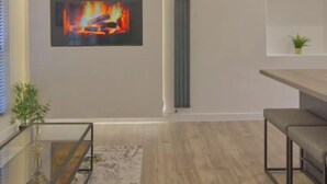 En moderne stue med pejs, et glasbord, et spiseområde med bænk og en potteplante.