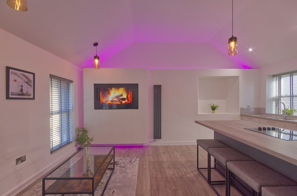 A modern kitchen with a bar area, pendant lighting, and a large painting of a fire.