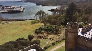 A coastal landscape with a castle-like structure, a body of water, and a distant ship. - Harris (Isle of Lewis)