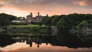 A castle-like building with a moat in front, surrounded by trees and a cloudy sky. - Harris (Isle of Lewis)
