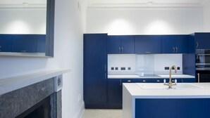 A modern kitchen with dark blue cabinets, a white countertop, and a central island with a sink and faucet. - Ranol (Isle of Lewis)