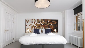 A modern bedroom with a large bed, a decorative wall panel, bedside lamps, and a window with a view. - Airinis (Isle of Lewis)