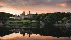 A castle with a moat, surrounded by lush greenery and a calm lake reflecting the structure. - Airinis (Isle of Lewis)