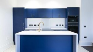 A modern kitchen with a central island, white cabinets, and dark blue accents. - Airinis (Isle of Lewis)