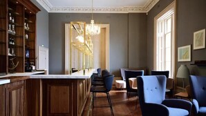 A dining area with a wooden bar, blue upholstered chairs, and a chandelier. - Airinis (Isle of Lewis)