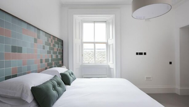 A bedroom with a large bed, a tiled headboard, a window, and a radiator. - Sutherland (Isle of Lewis)