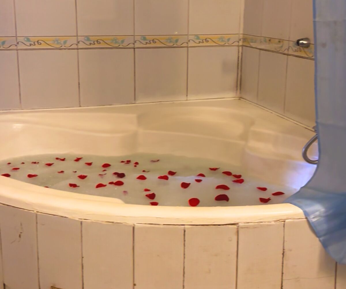 A corner bathtub with water and rose petals.