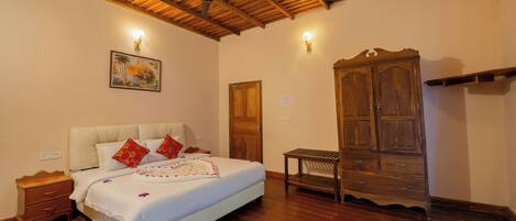A bedroom with a wooden ceiling, a bed with white bedding and red pillows, a wooden wardrobe, and a small table.