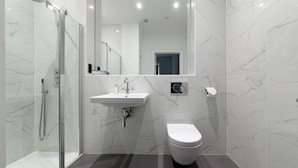 Un baño moderno con ducha de vidrio, lavamanos blanco y un inodoro.