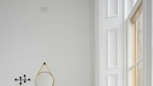 Una habitación con un sofá negro, un banco amarillo tapizado y un radiador blanco.