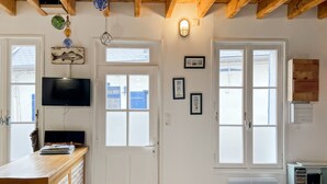 Et værelse med træloft, fjernsyn monteret på væggen, et skrivebord med papirer, en stol og et vindue med udsigt til bygninger.