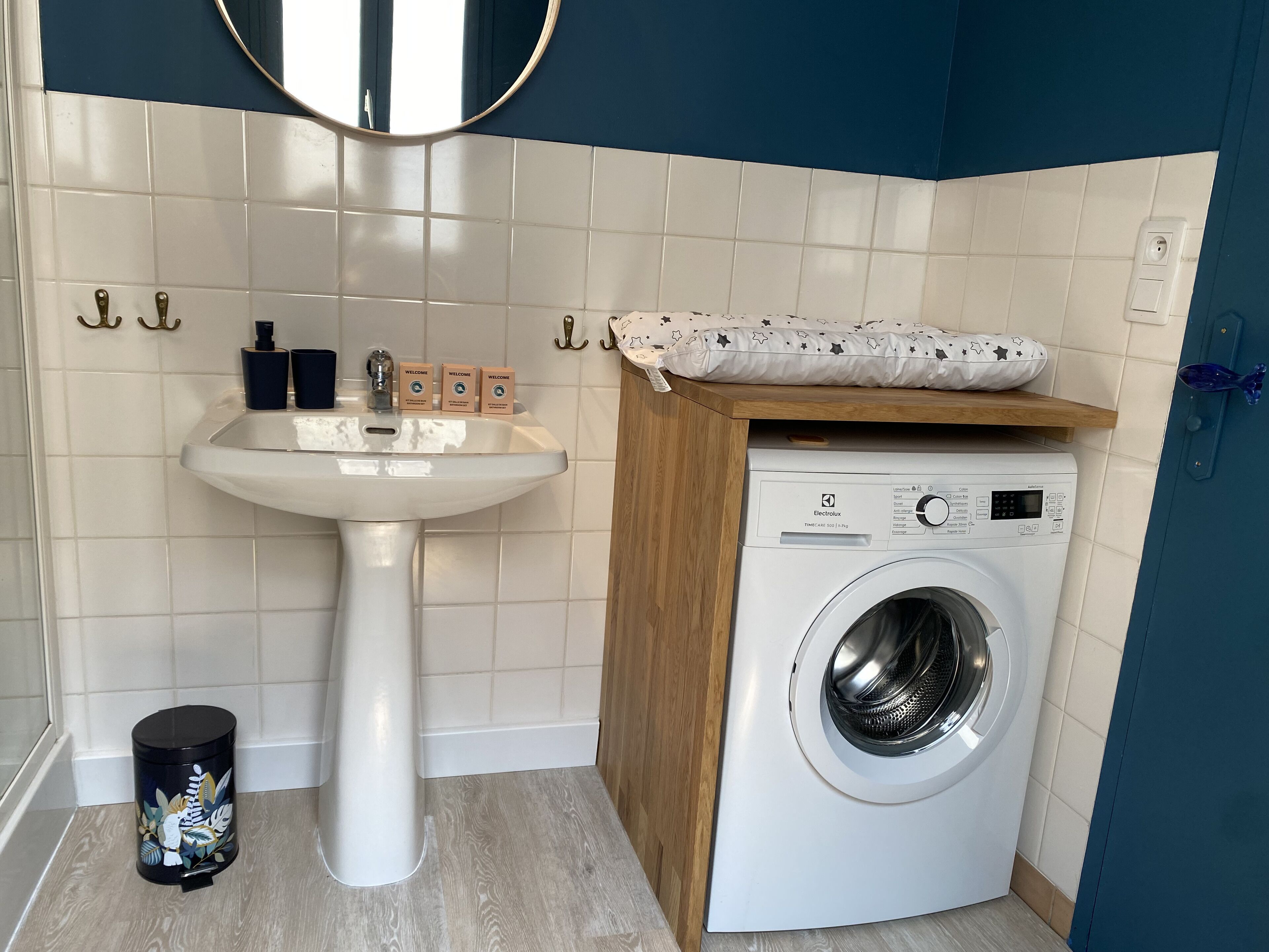 A compact bathroom with a pedestal sink, a washing machine, and a small trash bin.