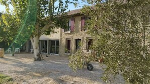 Een landelijke woning met een grindpad, een overdekt terras en een boom die schaduw geeft.