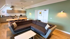 A modern living room with a sectional sofa, a dining table, and a kitchen in the background. - Northstar - 4 Bed Luxury Apartment (Wick)